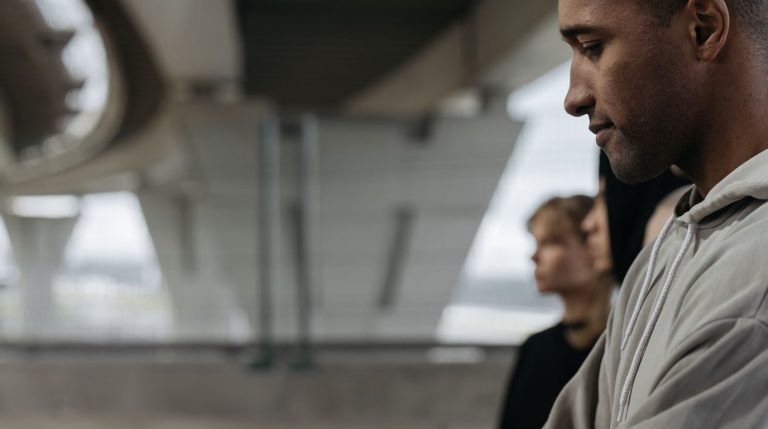A man stands apart from a small group, looking away, in soft overcast daylight.