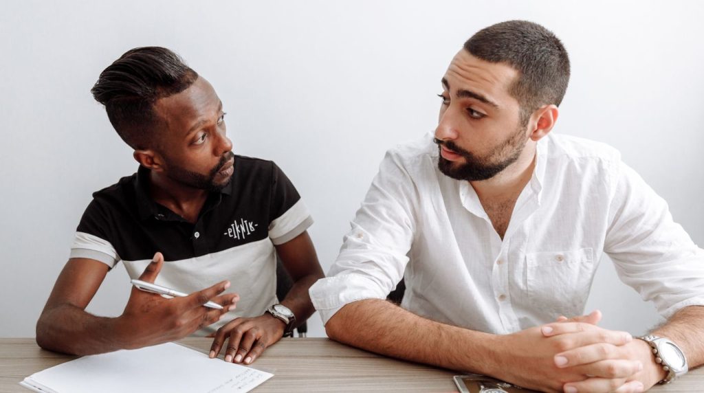 A man talks with a counsellor across a table, notes in front of them, in a calm daylit room.